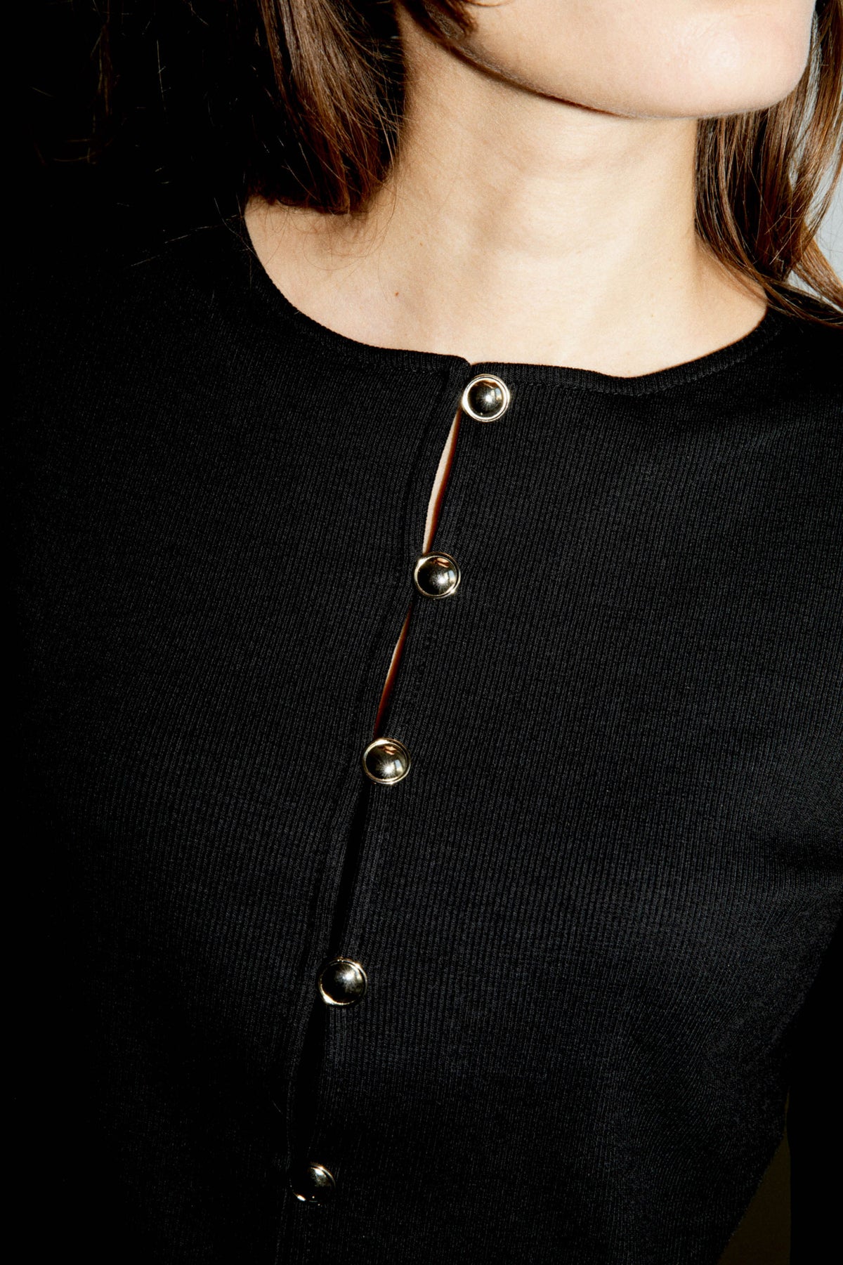 Gros plan sur les boutons dorés et la maille en coton biologique d'un cardigan noir pour femme, fabriqué au Portugal.